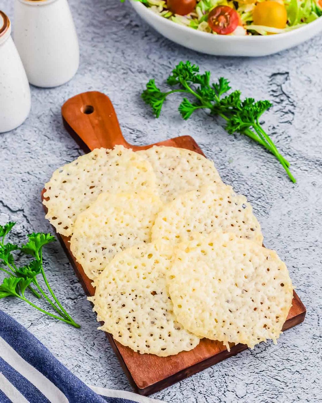 Cheese crackers on a cutting board next to a bowl of salad.
