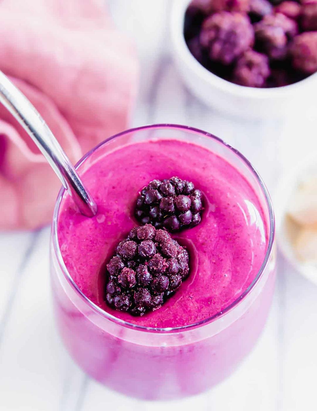 A blackberry smoothie in a glass with a metal straw.