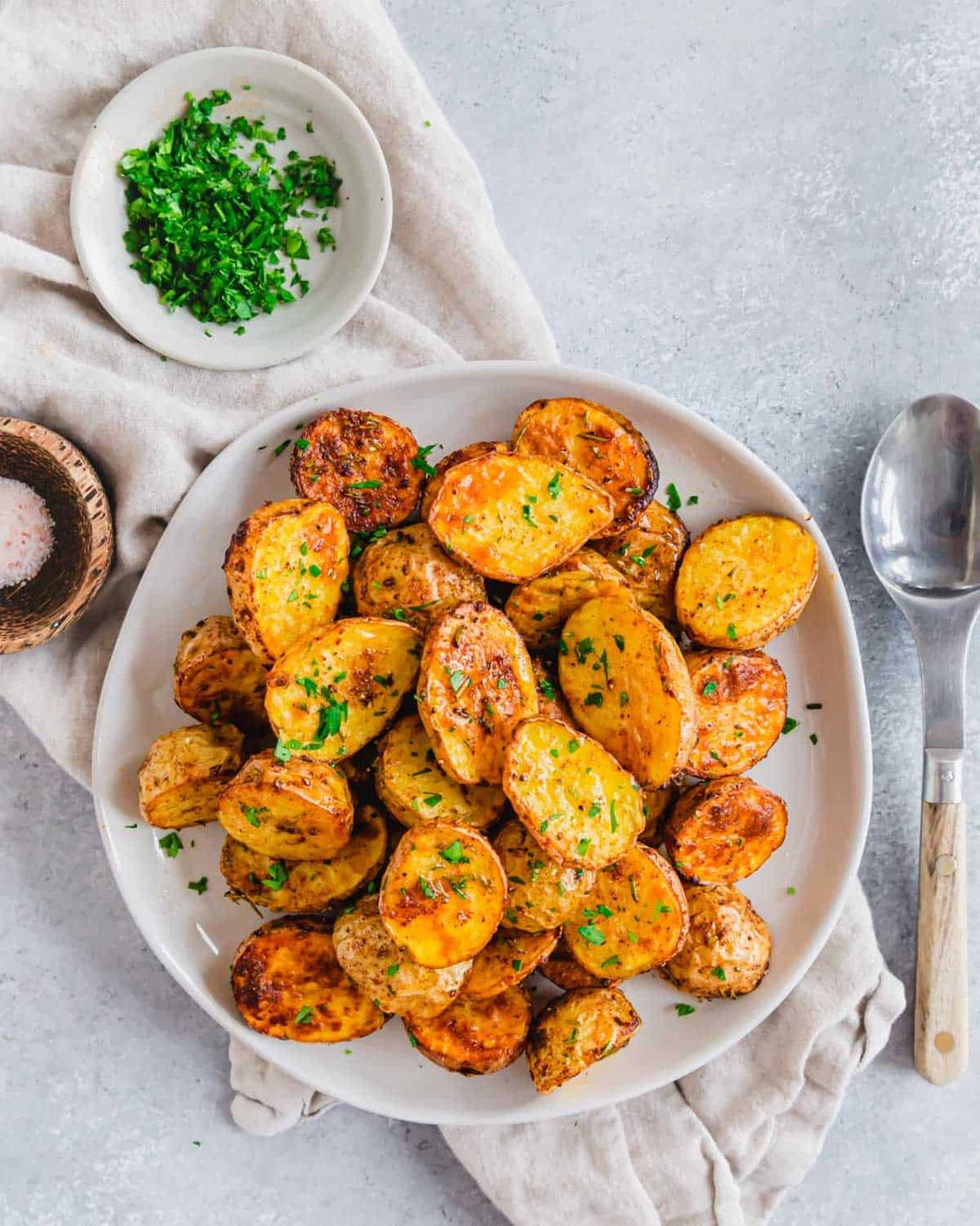Air fried roasted baby potatoes garnished with fresh parsley on a plate with a serving spoon.