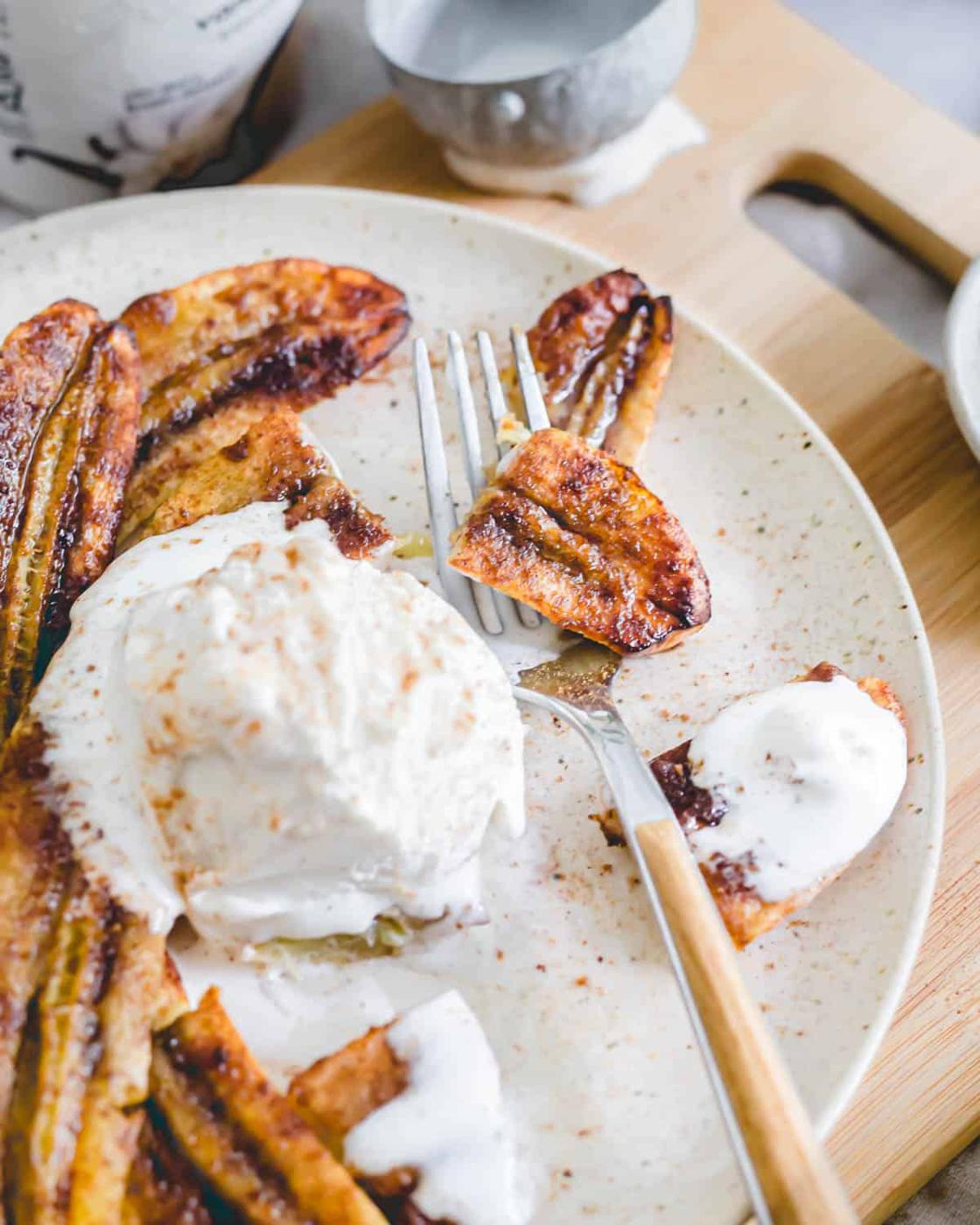 Sweet caramelized bananas in the air fryer cut into pieces on a plate with vanilla ice cream and a fork.