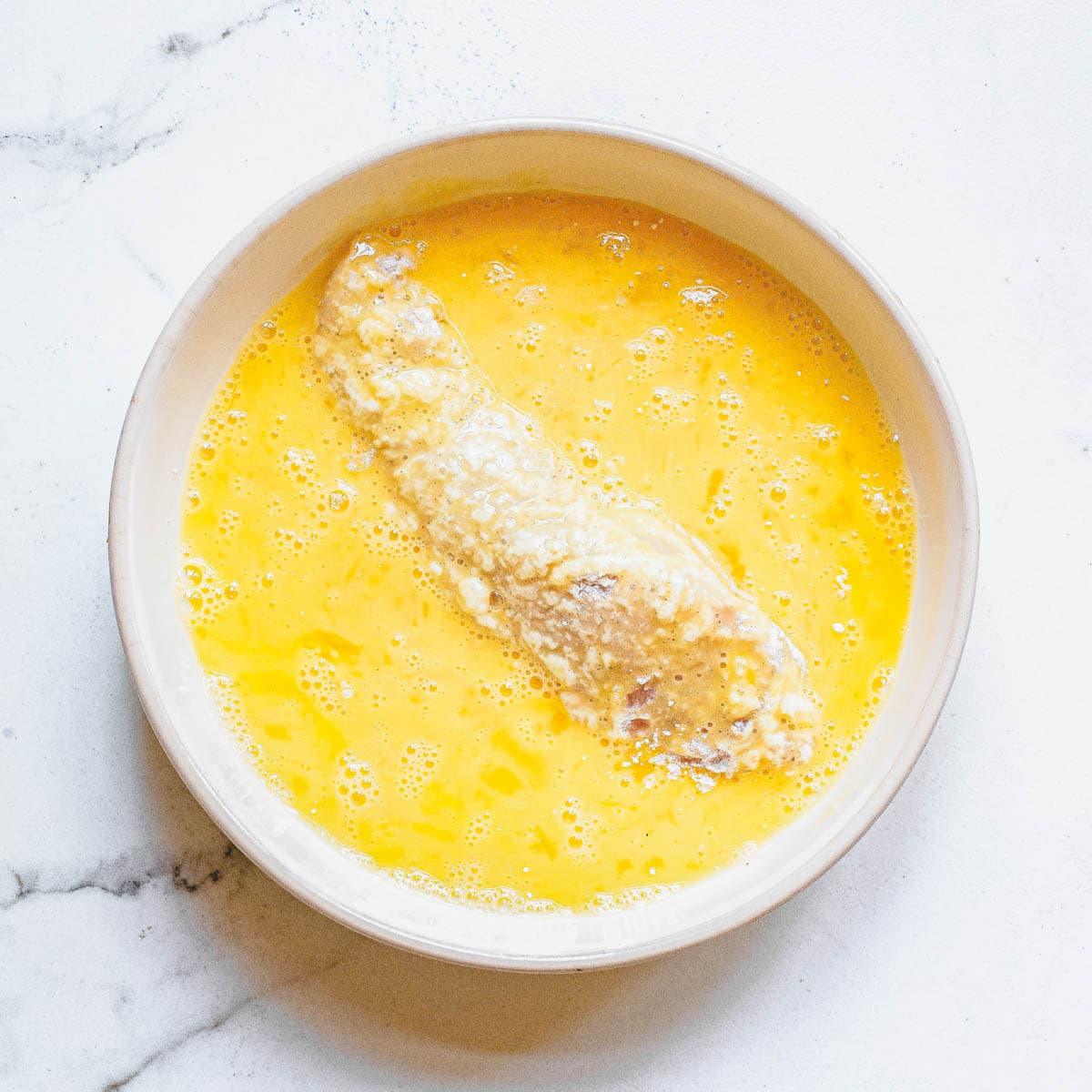 Dredging chicken tenders in an egg wash.