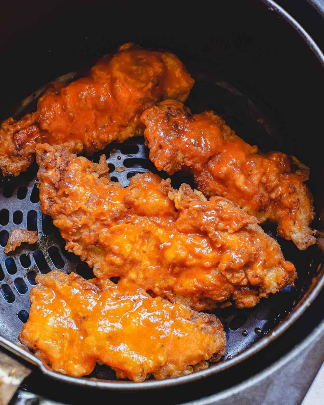Crispy air fried buffalo chicken strips in the air fryer basket.