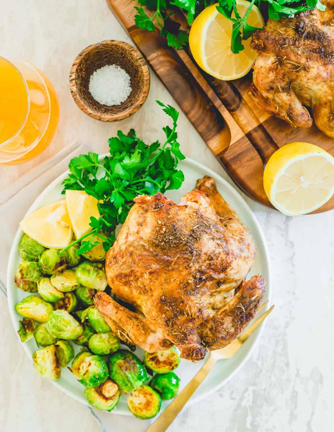Cornish hen roasted in the air fryer on a plate with Brussels sprouts and lemon.
