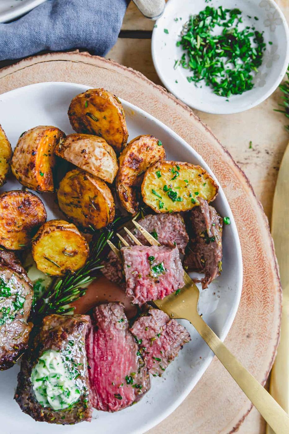 Tender, juicy piece of air fryer filet mignon on a fork served with baby potatoes and compound butter.