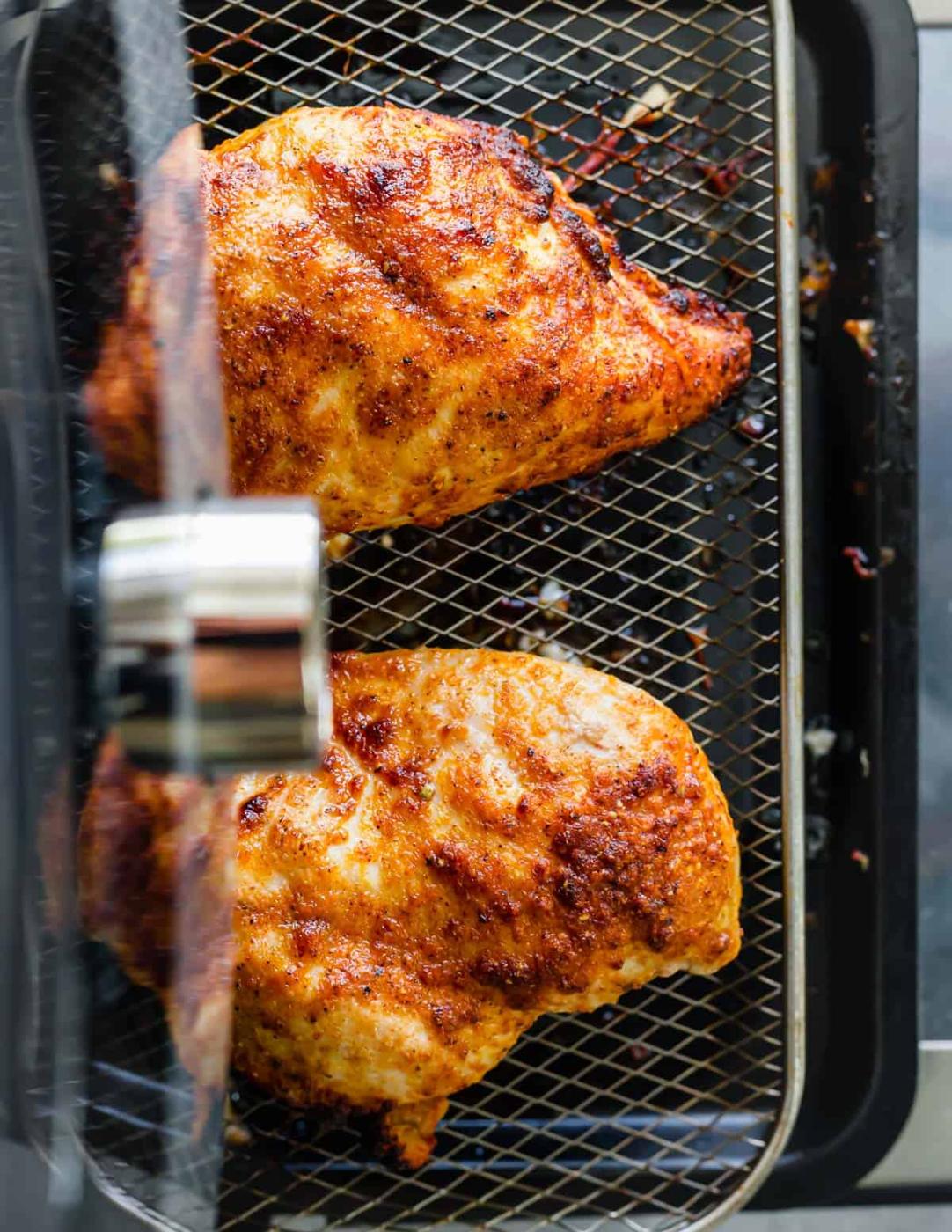Cooked frozen chicken breasts on the tray of an air fryer.