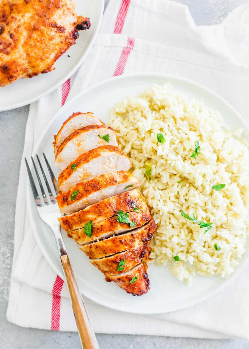 Frozen chicken breasts cooked in an air fryer sliced on a plate with white rice and parsley.