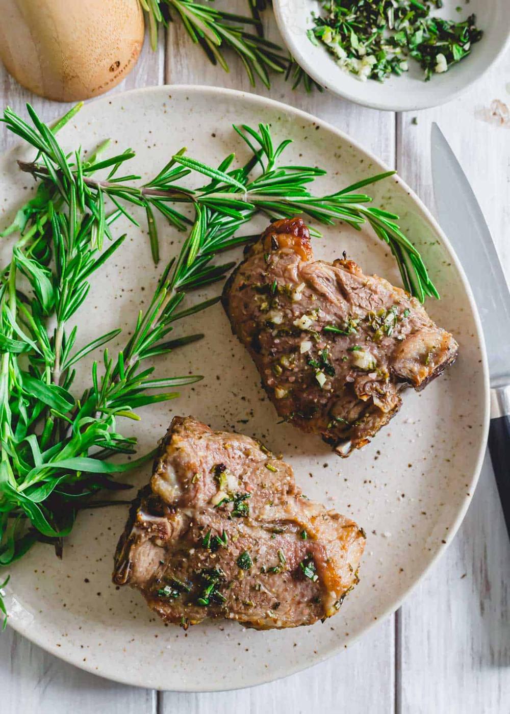Lamb chops cooked in the air fryer on a serving plate with fresh herbs and knife.