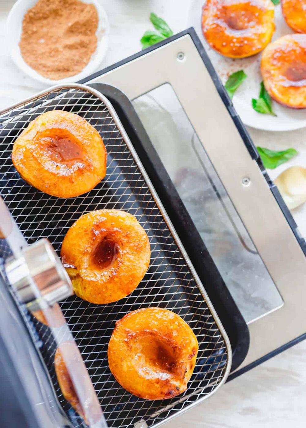 Air fried peach halves on a tray in a Pampered Chef air fryer.