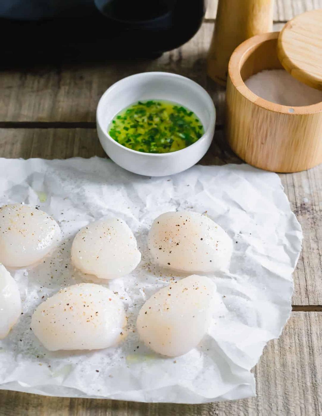 Fresh sea scallops on parchment paper with salt and pepper.