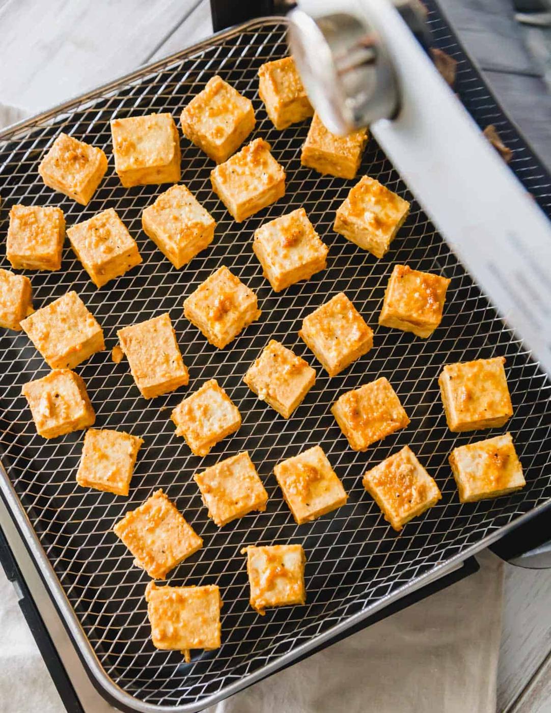 Cubed tofu with tamari, olive oil, garlic and onion powder on a Pampered Chef air fryer tray.