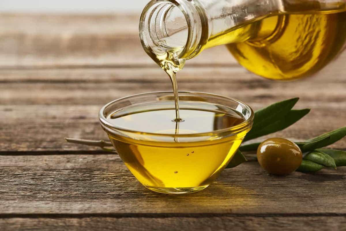 Olive oil being poured into a glass on a wooden table.