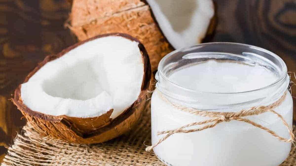 A jar of coconut oil with a half coconut shell in the background.