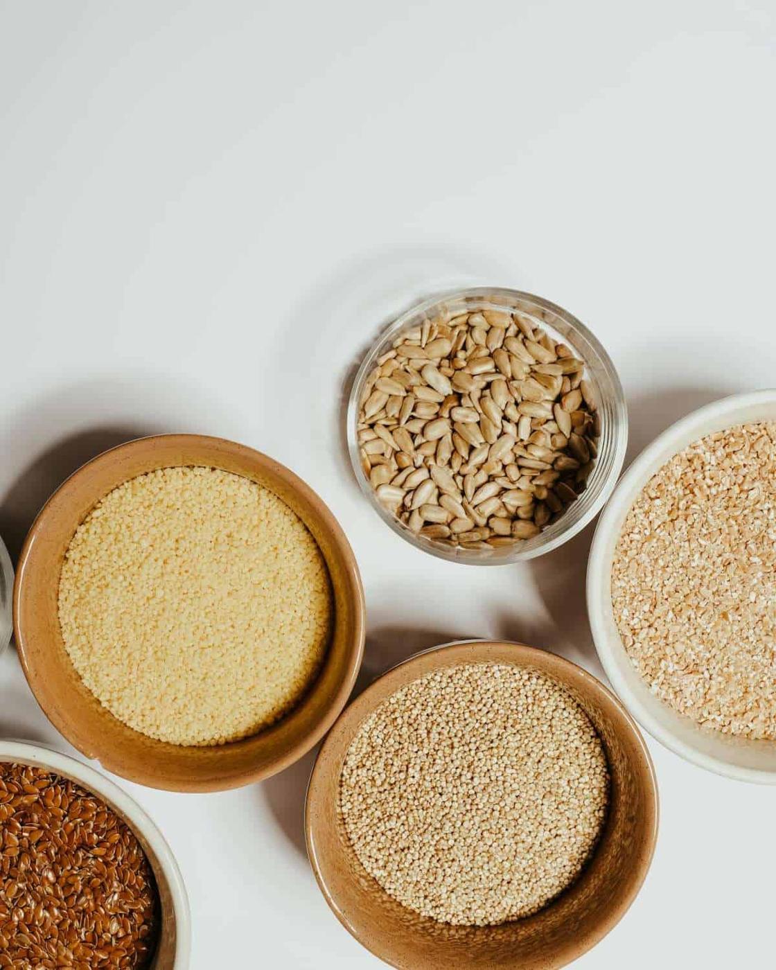 Various ancient grains and seeds neatly arranged in bowls on a white surface.