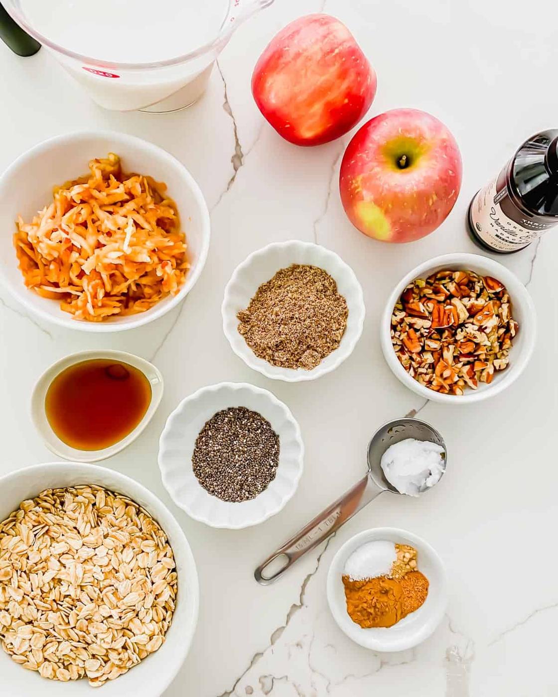 Ingredients to make apple cinnamon oatmeal: rolled oats, chia seeds, ground flaxseed, cinnamon spices, chopped pecans, grated apple, vanilla extract, maple syrup and coconut oil.