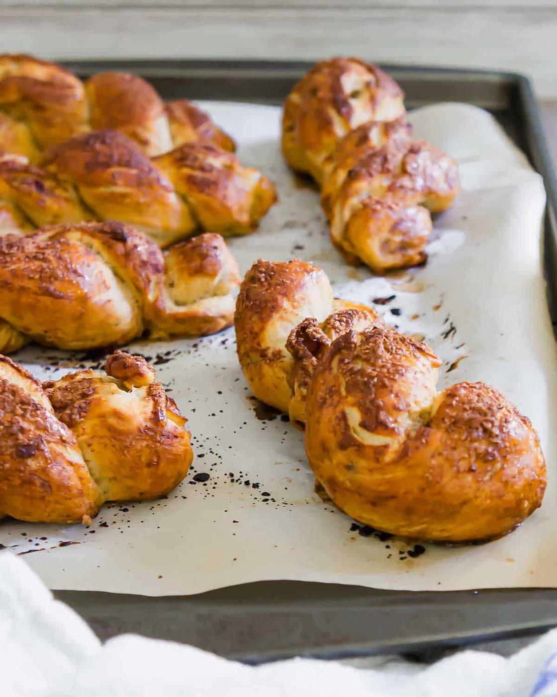 Golden-brown pretzel twists resting on a parchment-lined baking sheet, freshly baked and sprinkled with coarse salt.