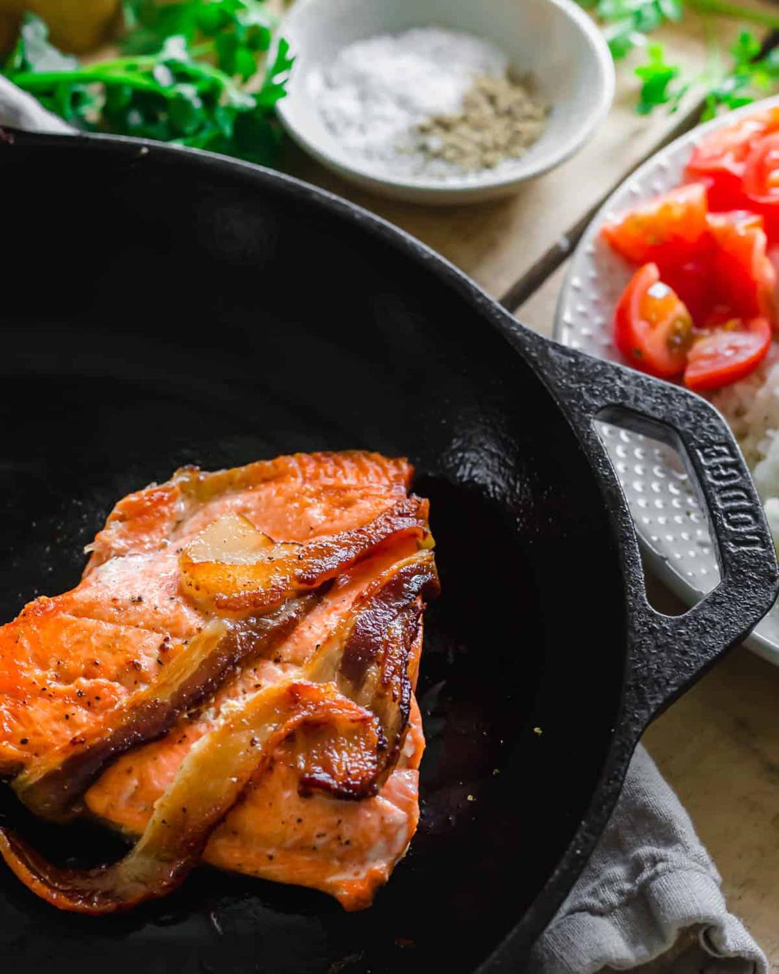 Close up of salmon cooked in a cast iron skillet wrapped in bacon.