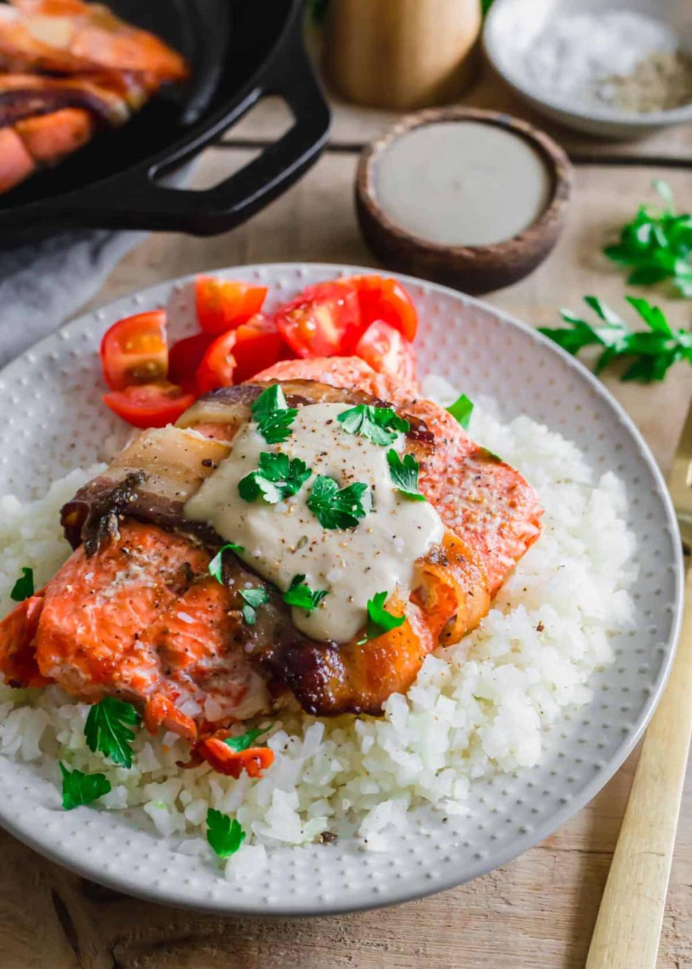 Oven baked bacon-wrapped salmon recipe topped with tahini sauce and fresh cilantro on a white plate.