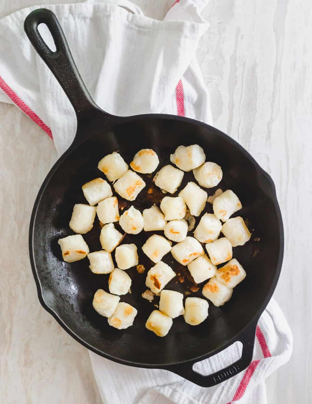 Cauliflower gnocchi browned in a skillet with olive oil.