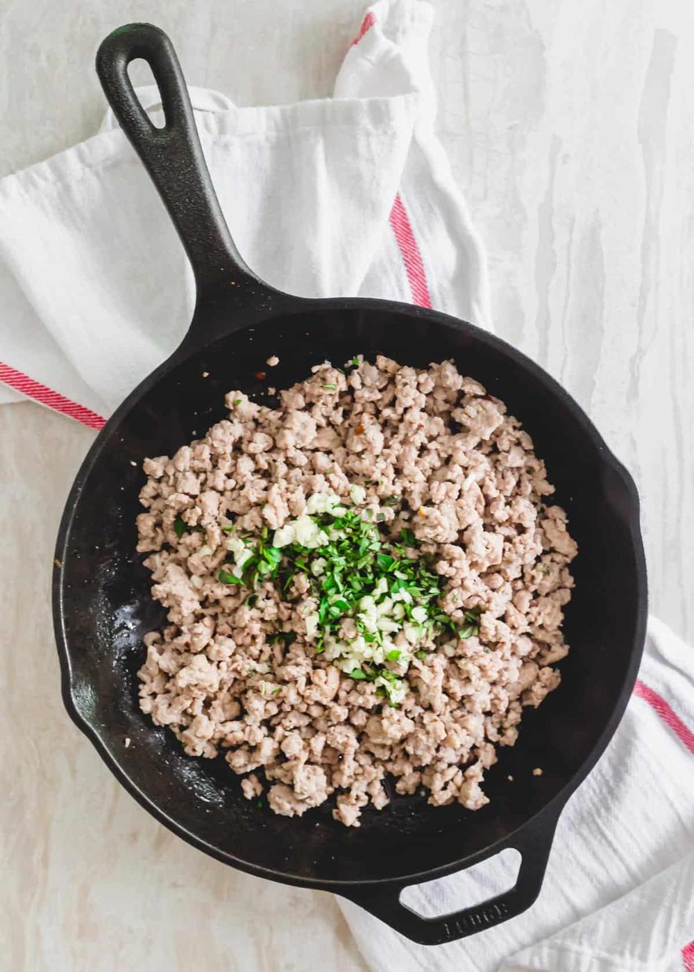 Cooked ground pork with fresh oregano, garlic, salt, pepper and red pepper flakes in a skillet.