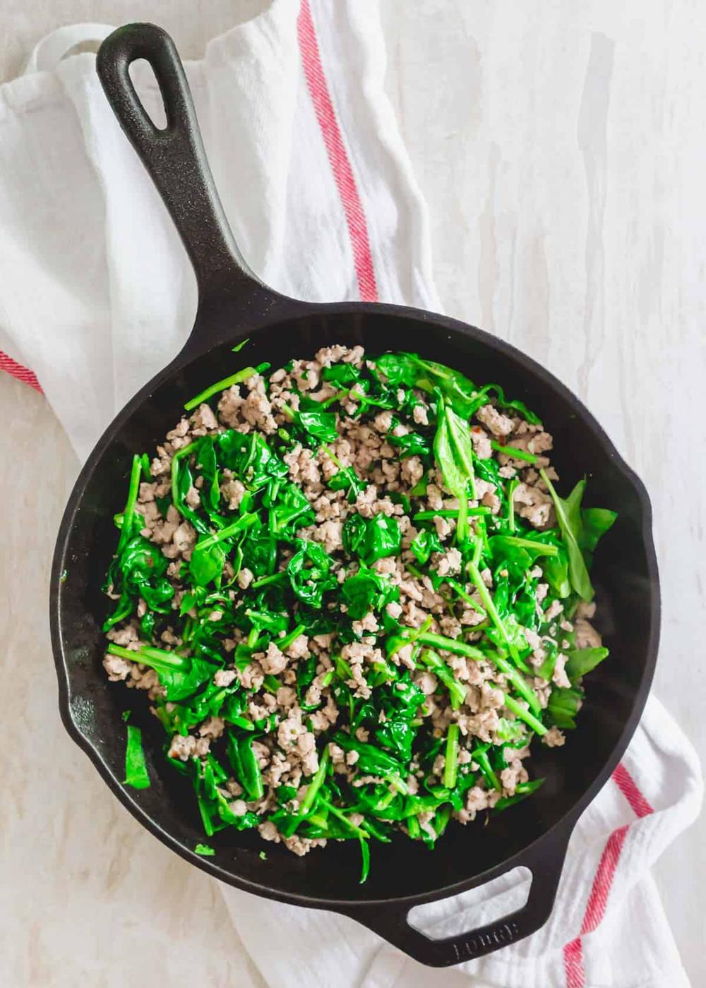Fresh spinach greens wilted into ground pork mixture for cauliflower gnocchi recipe in a skillet.