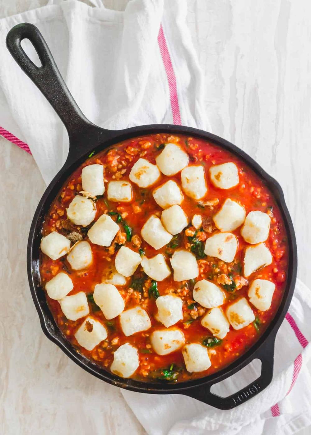 Cauliflower gnocchi in a skillet with crushed tomatoes, cooked ground pork and spinach.