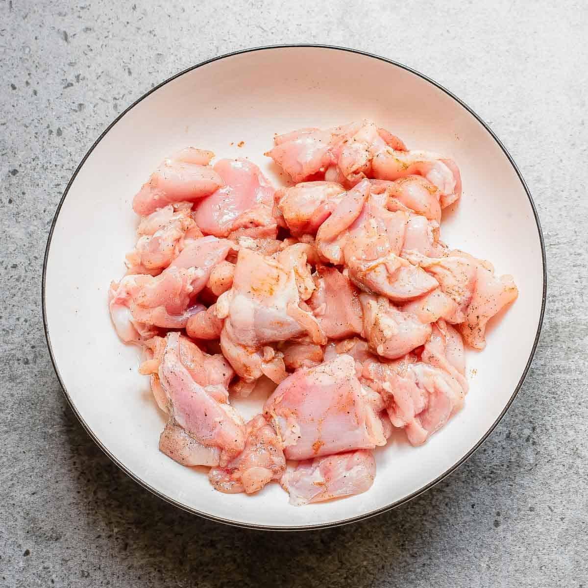 Cut up pieces of chicken thighs in a bowl with spices.