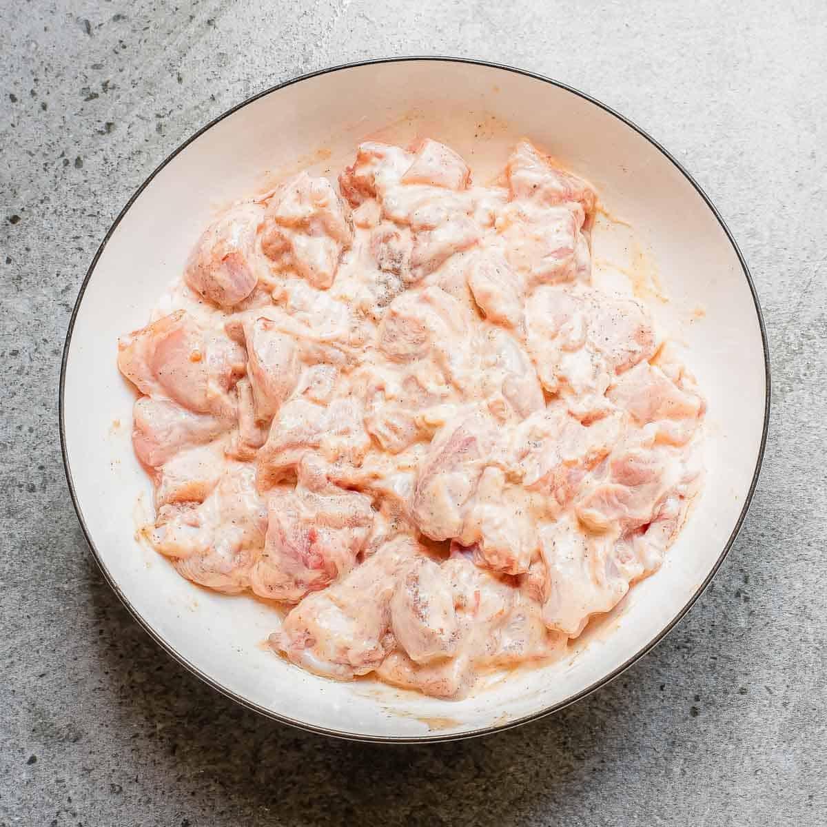 Chicken thigh pieces marinating in a bang bang sauce in a large bowl.