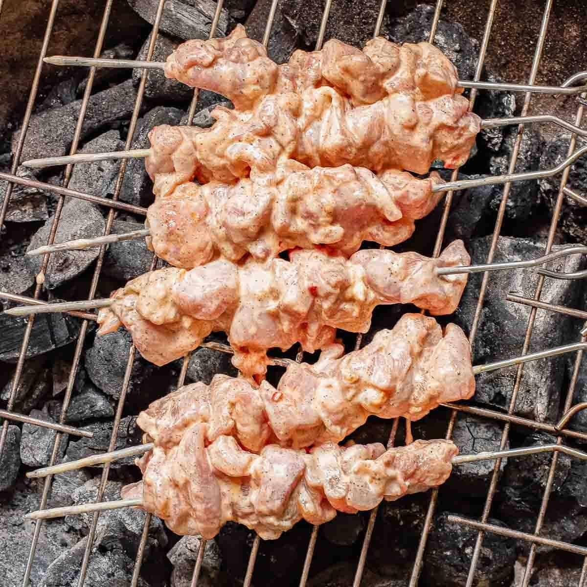 Chicken skewers coated in a creamy marinade on a charcoal grill.