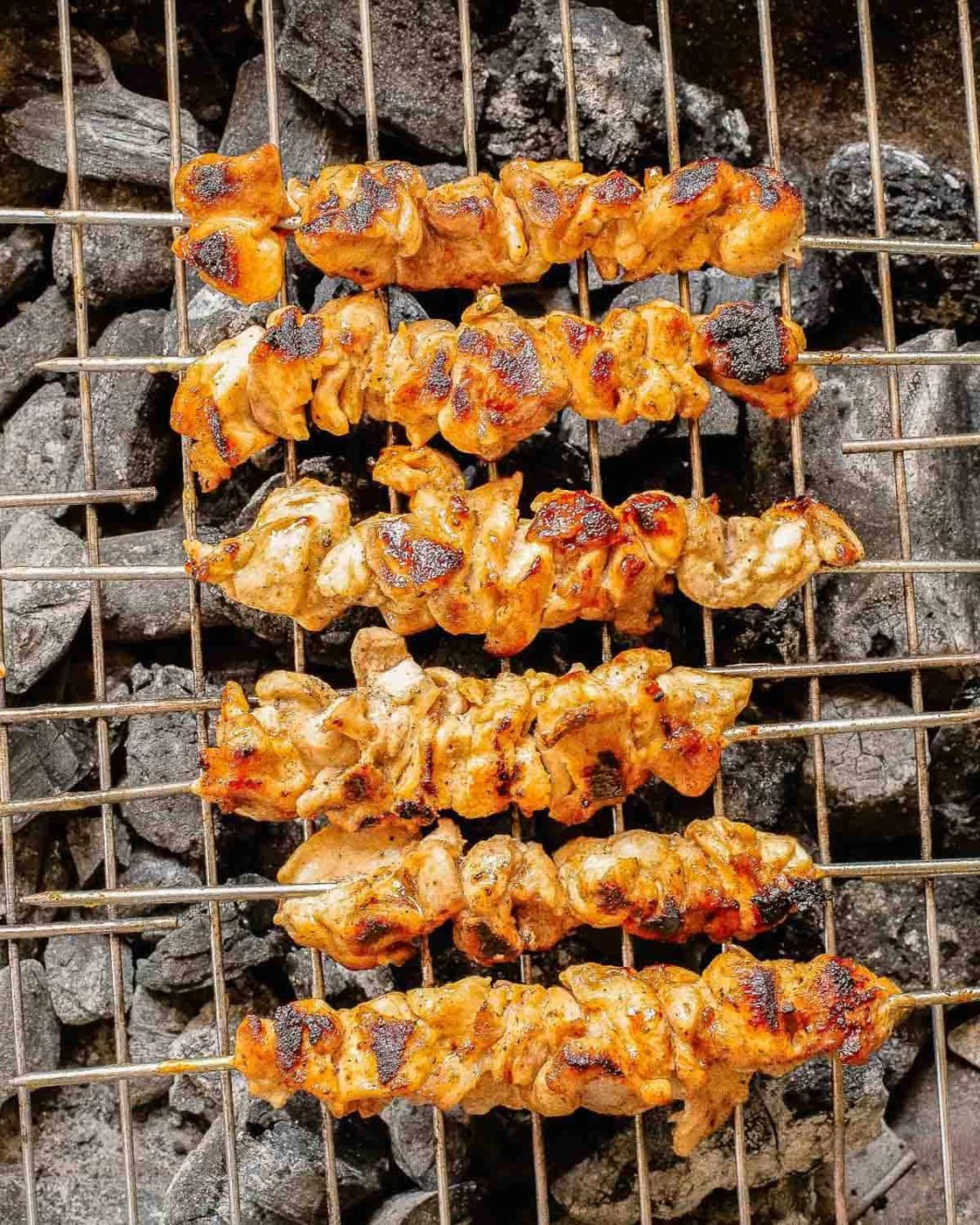 Cooked bang bang chicken skewers on a charcoal grill.