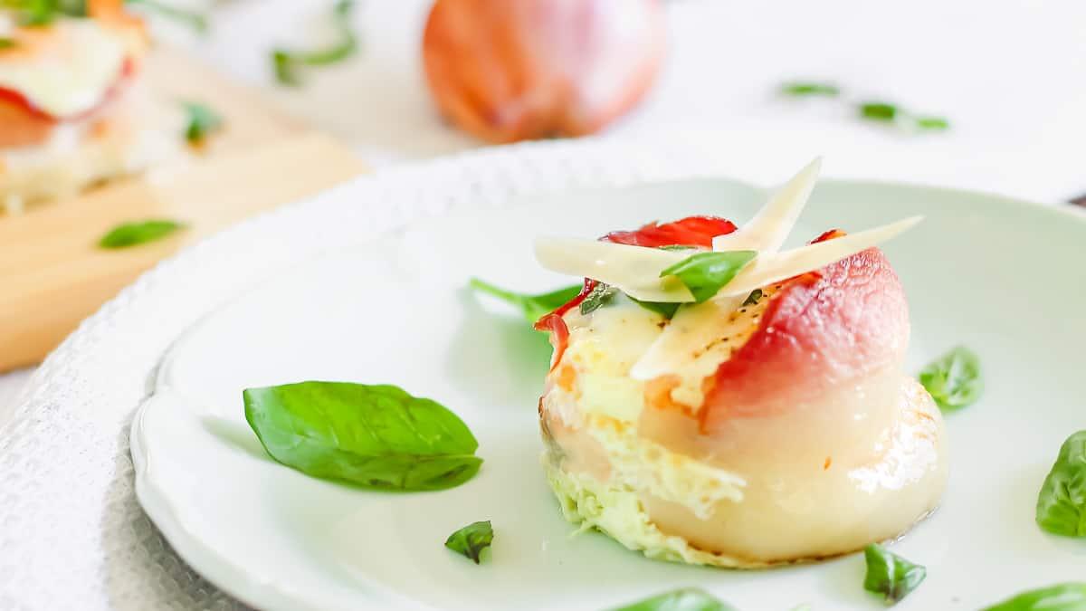 Bacon wrapped egg cups topped with shavings of parmesan cheese and fresh basil on a light blue plate.