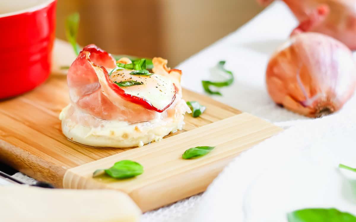 Bacon egg cup with basil and parmesan on a wooden surface.