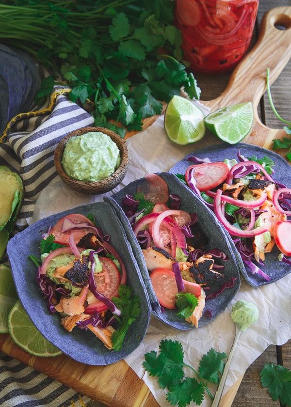 These blackened salmon tacos are topped with quick pickled radishes and red onion, an avocado cilantro cream and served on blue corn tortillas for one amazing bite!