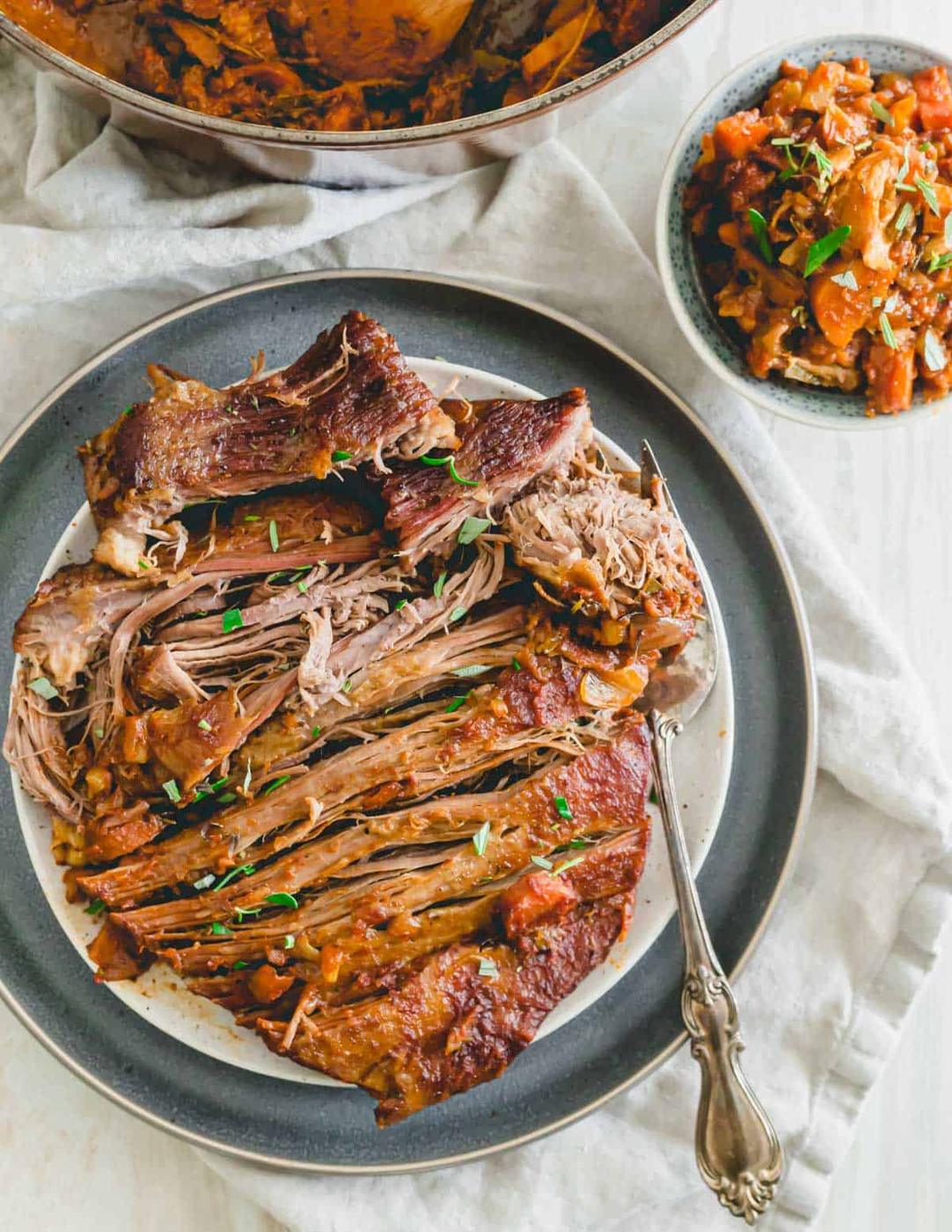Braised veal brisket shredded into pieces on a plate with a serving fork.