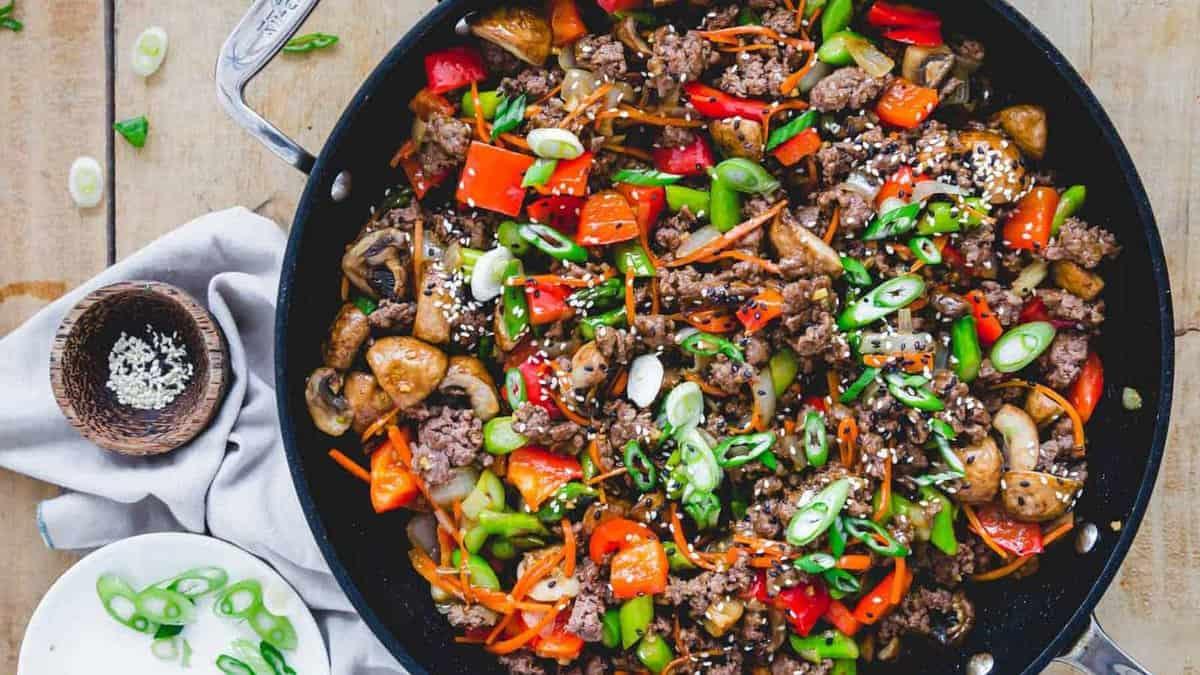 A skillet full of vegetables and beef on a wooden table.