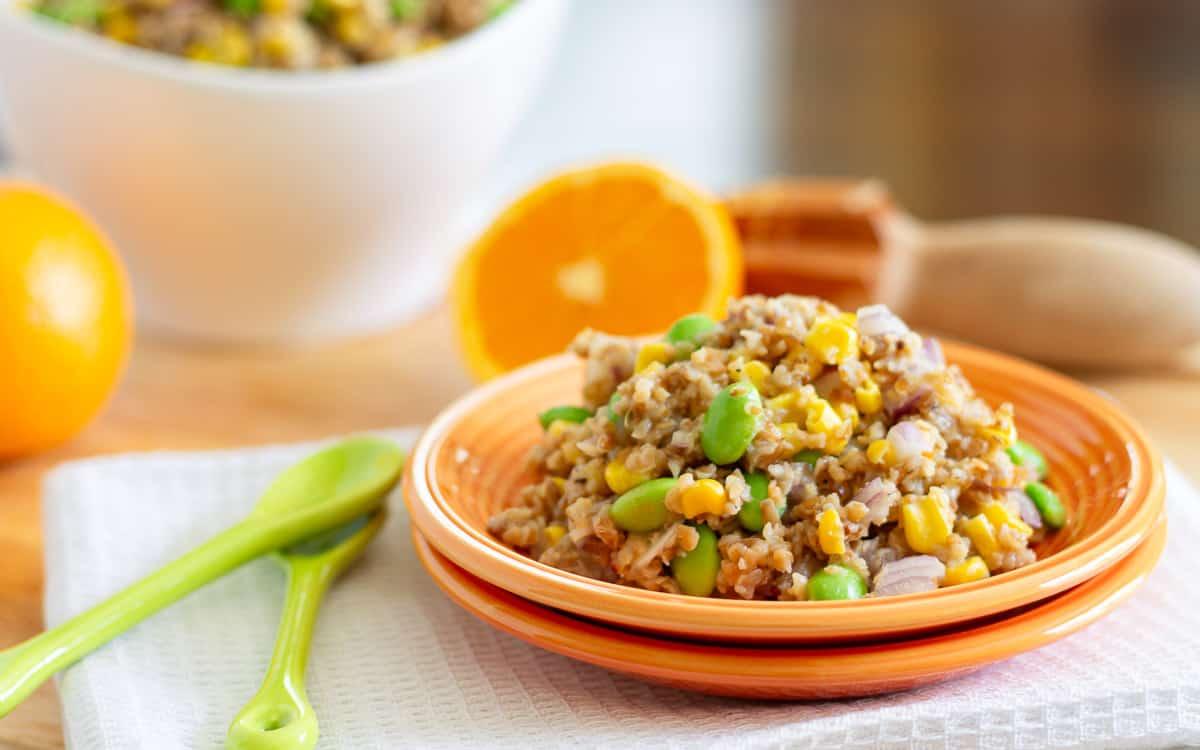 Bulgur salad with edamame, red onion and corn on orange plates.