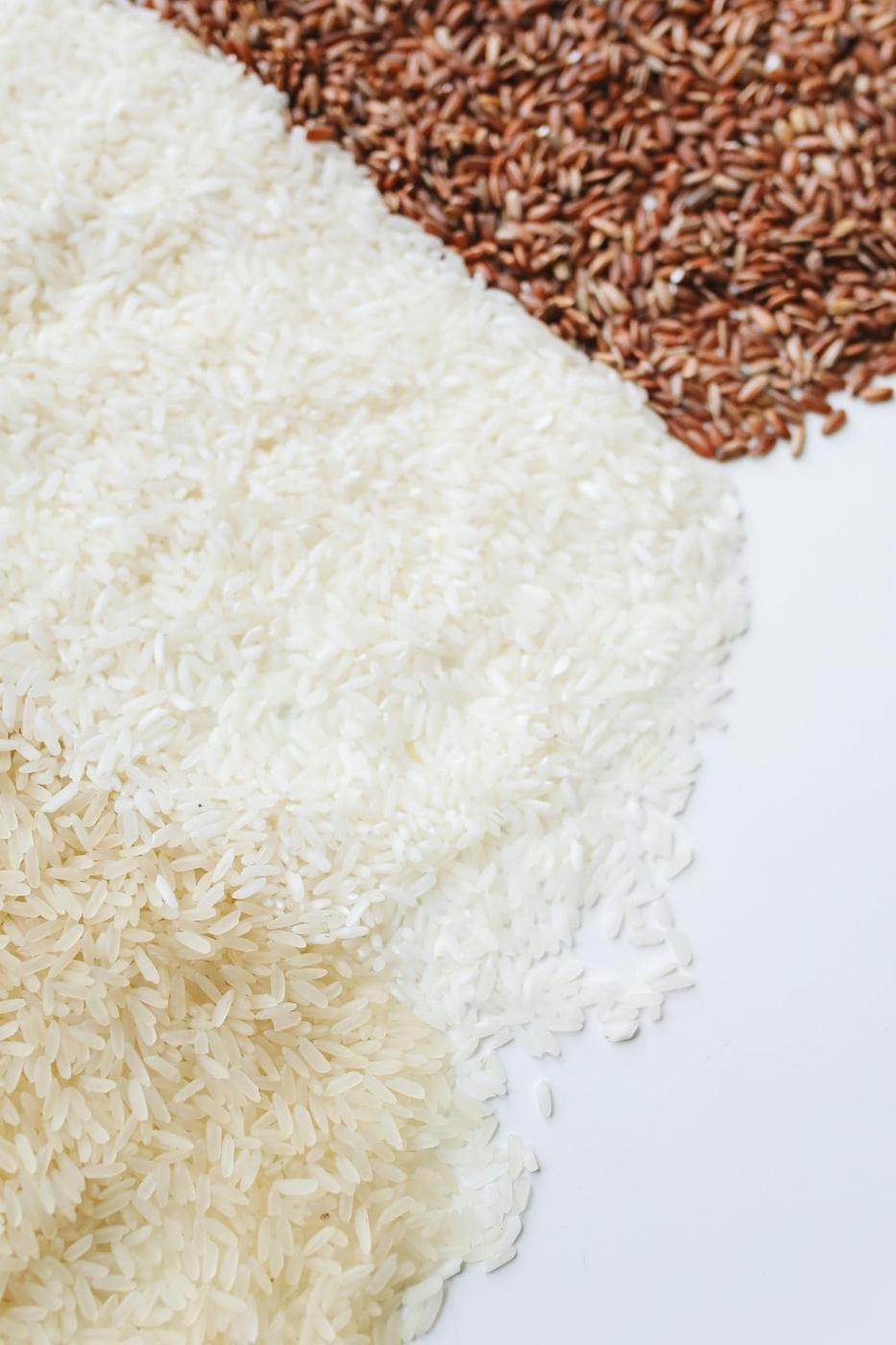 Two varieties of uncooked rice, white and brown, arranged in separate heaps on a white surface.