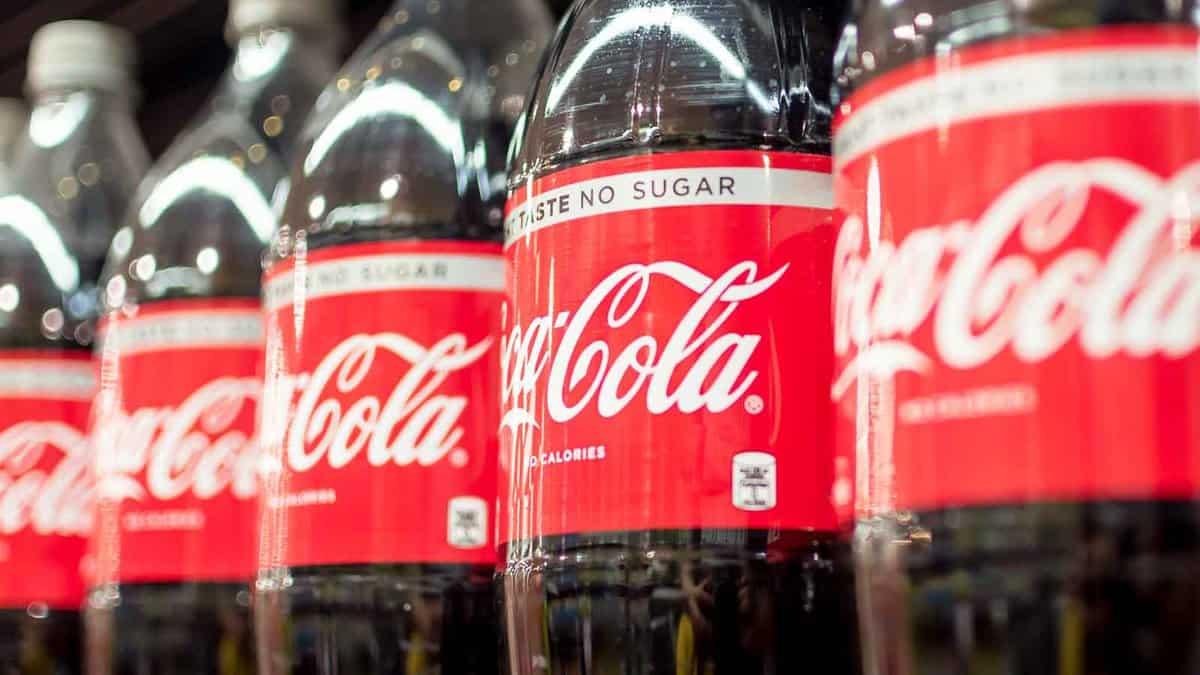 A row of coca cola bottles lined up on a shelf.