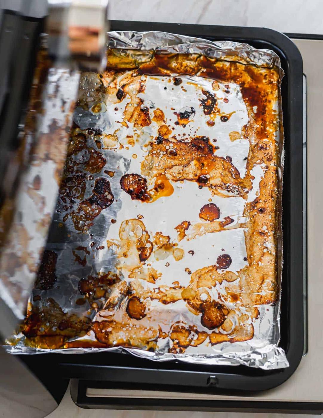 Tin foil lined grease tray in an air fryer oven after cooking.