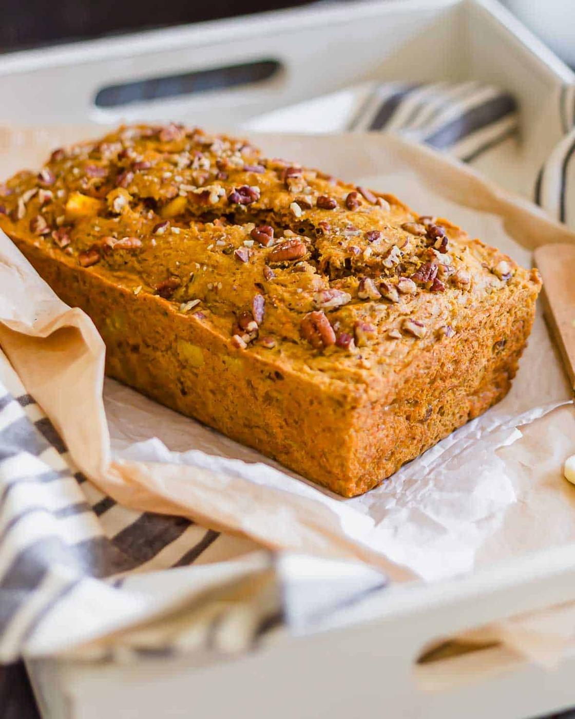Carrot bread loaf topped with pecans on parchment paper in a serving tray.
