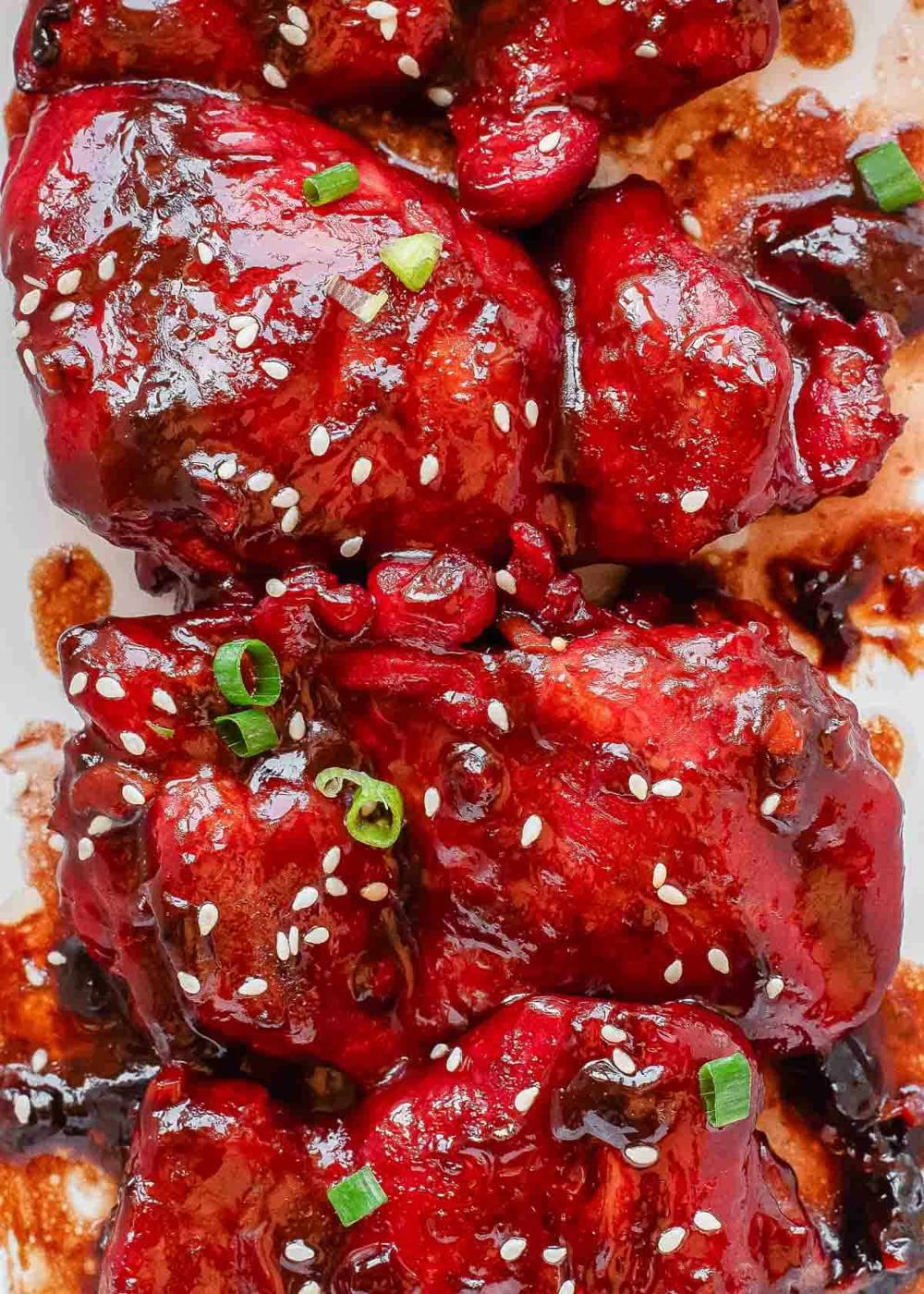 Close-up of glazed char siu chicken pieces topped with sesame seeds and chopped green onions, coated in a shiny, dark red sauce.