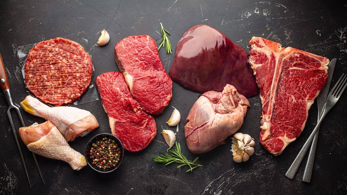 Various raw meats and poultry arranged with spices and herbs on a dark surface.