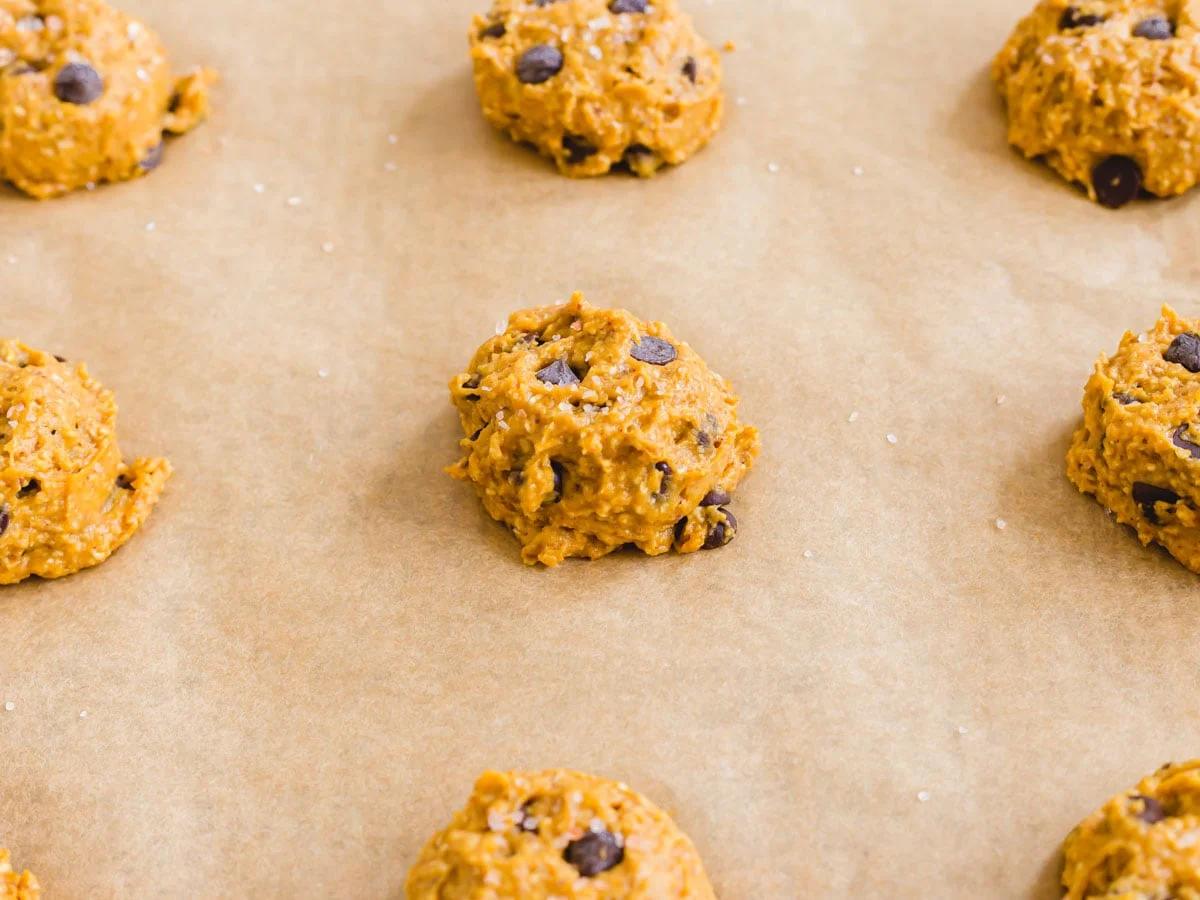 Pumpkin chocolate chip cookie dough scoops on a parchment lined baking sheet.