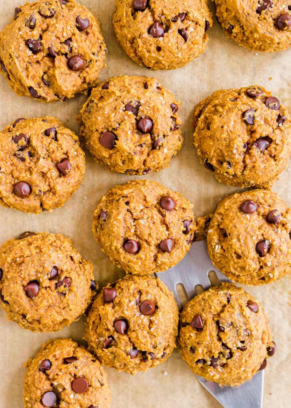 Soft baked vegan pumpkin chocolate chip cookies on a baking sheet with parchment paper topped with coarse sea salt.
