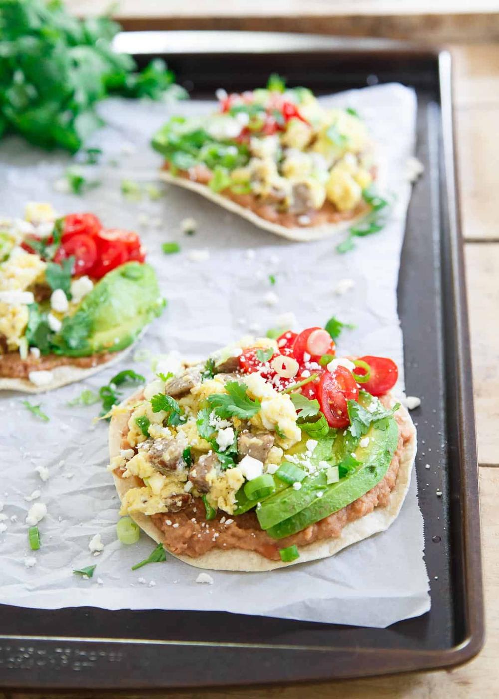 These breakfast tostadas include chicken sausage scrambled eggs piled high on a refried bean base. Avocado, tomatoes and cotija top it all off!