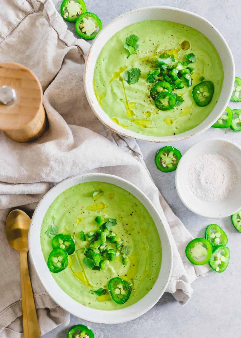 Cold avocado soup in bowls garnished with jalapeño and cilantro.
