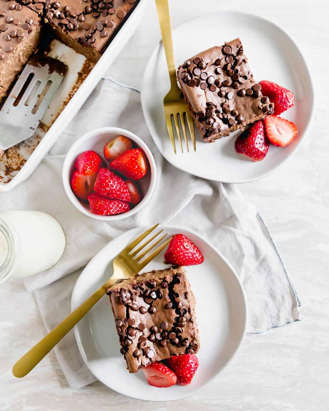 Two slices of baked chocolate oats on plates garnished with fresh strawberries for serving.