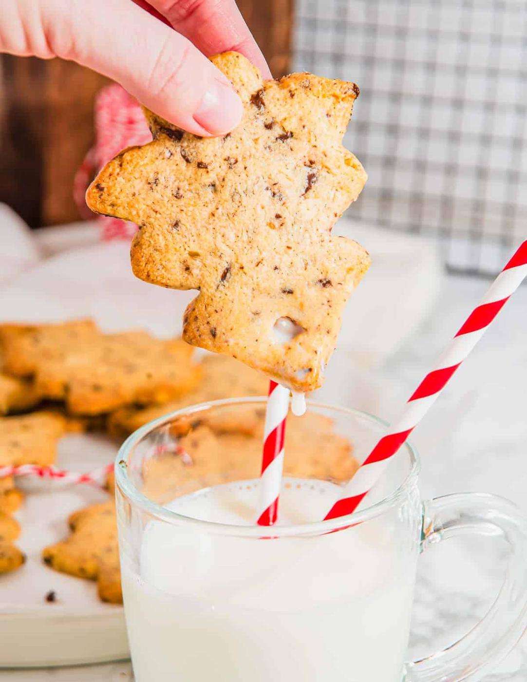 Dunking a Christmas tree cookie in a glass of milk with two straws in it.