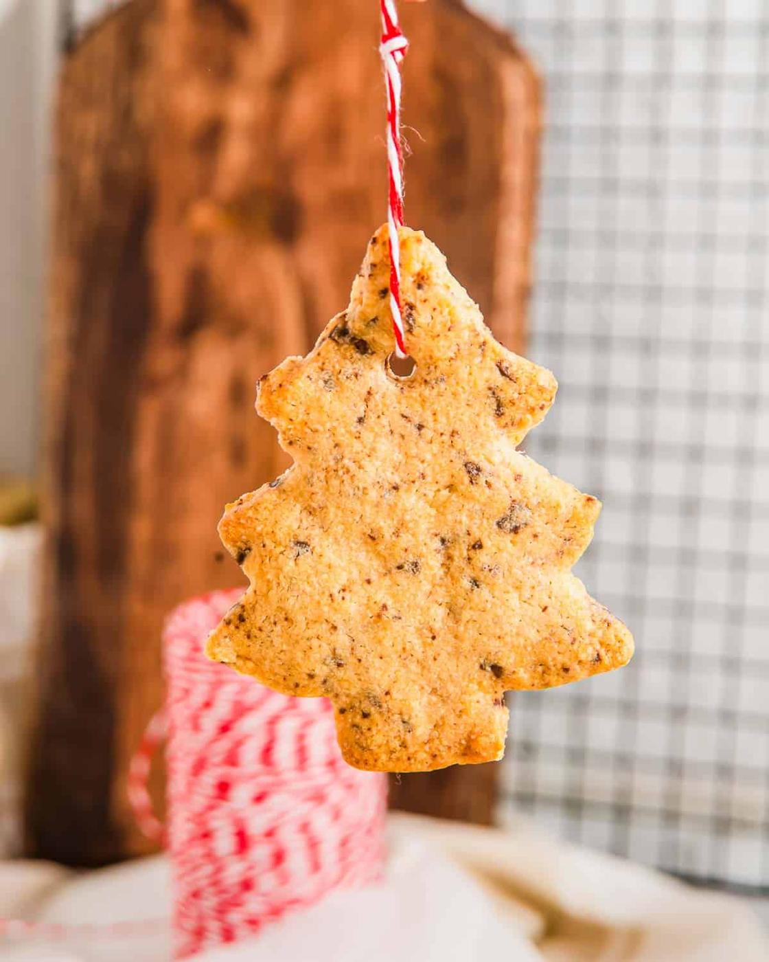 A Christmas tree cookie hanging by string with a spool of string in the background.