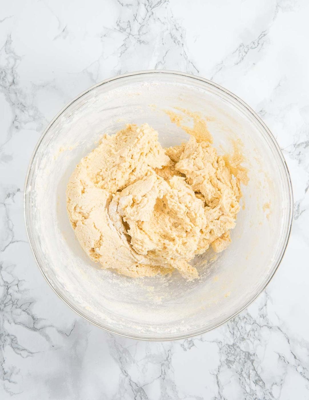 Cookie batter in a glass bowl on a marble surface.