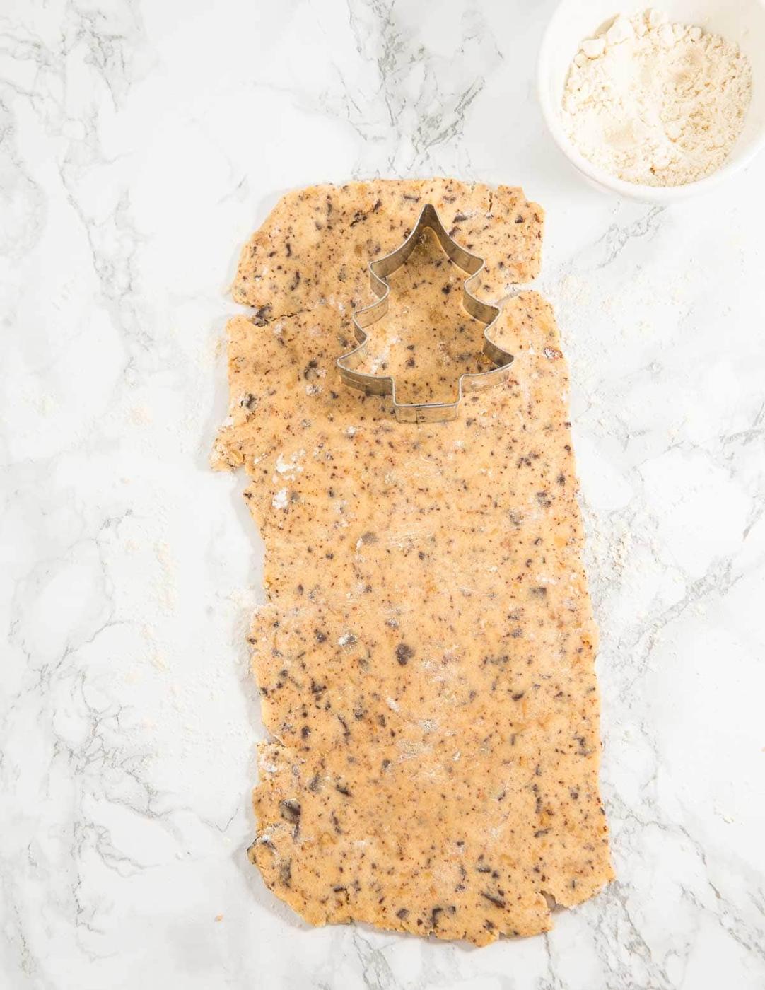 A Christmas tree cookie cutter sitting atop of rolled out cookie dough on a marble surface.